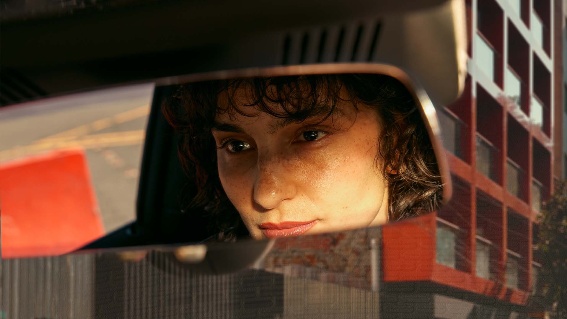 Rear-view mirror reflecting part of a person and urban buildings